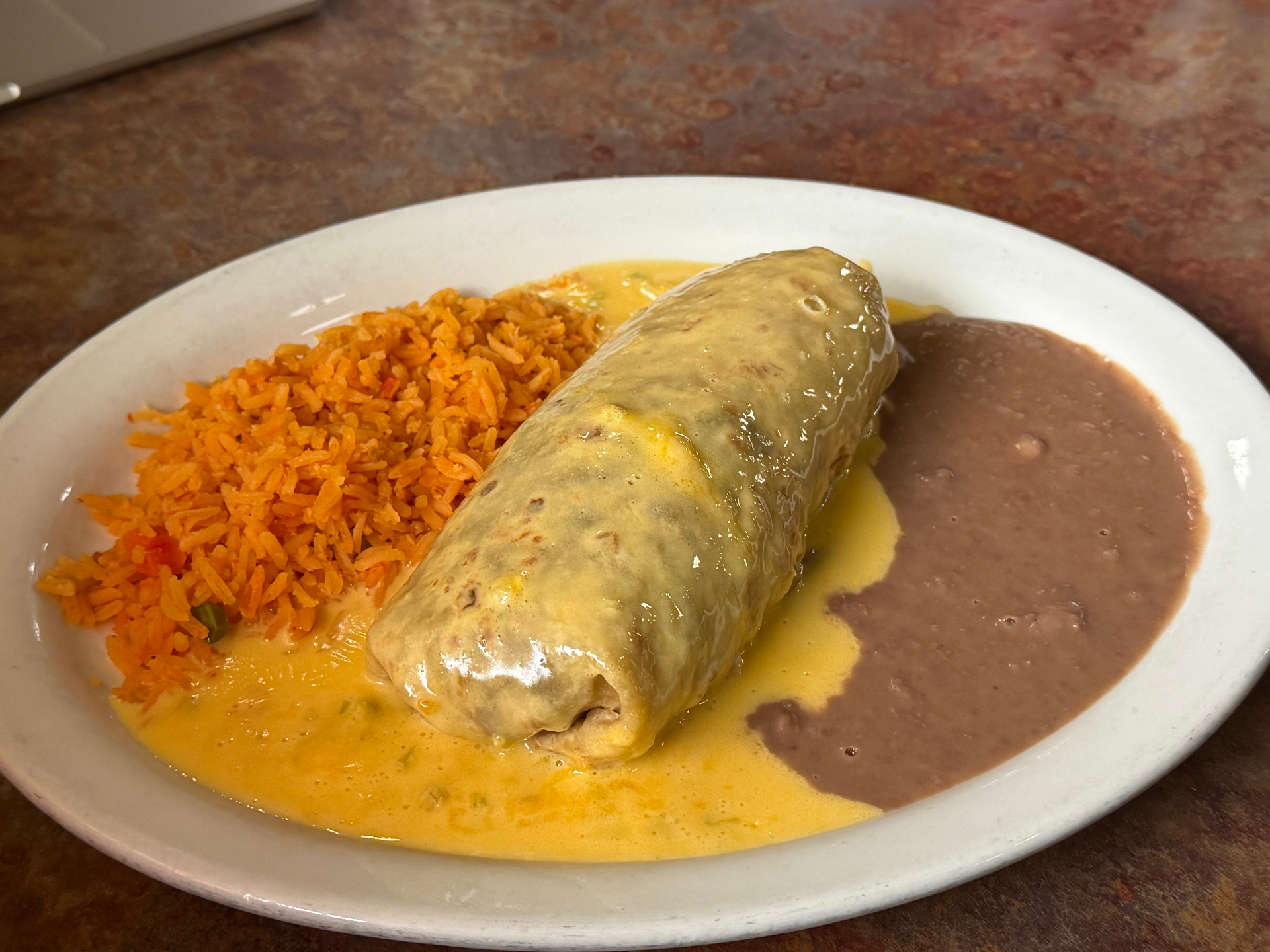 Burrito smothered in golden queso cheese sauce, served with Mexican red rice and refried beans.