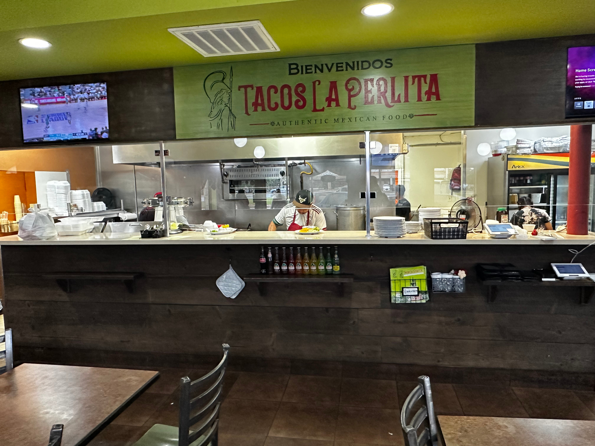 The storefront and dining room of Tacos La Perlita on Harvey Road, with the red restaurant signage above the entrance.