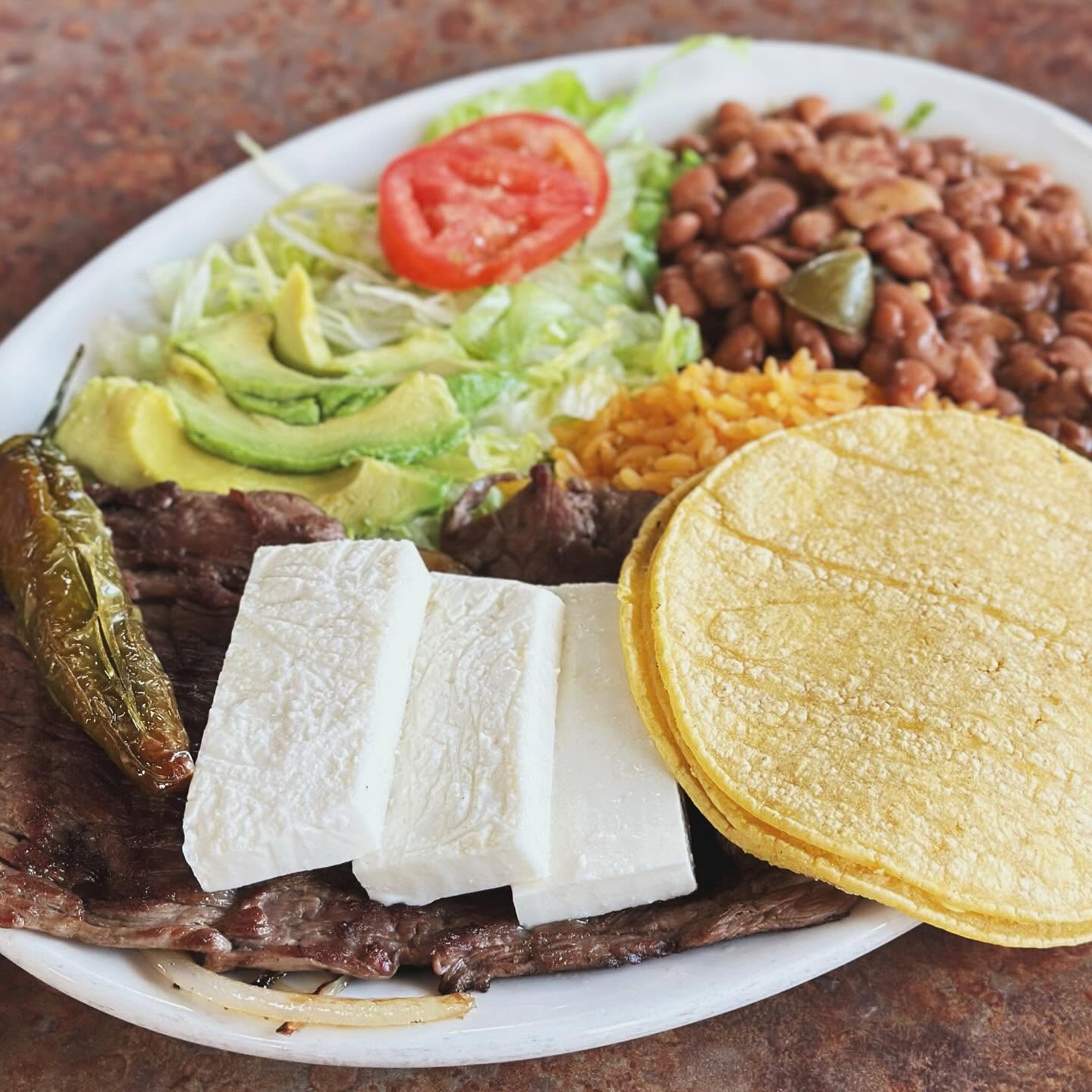 Carne asada with grilled onions, slices of queso fresco, avocado, beans, and corn tortillas.